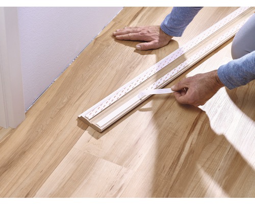 Bevestigen van een plint met tape op een houten vloer.