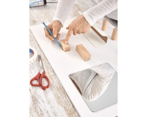 Persoon markeert met een potlood de positie van een houten blok op een plank.