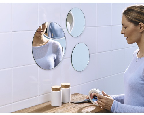 Vrouw bevestigt ronde spiegels met dubbelzijdige tape aan de muur, naast twee witte containers met kurken deksels