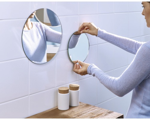Vrouw bevestigt ronde spiegel aan de muur in de badkamer