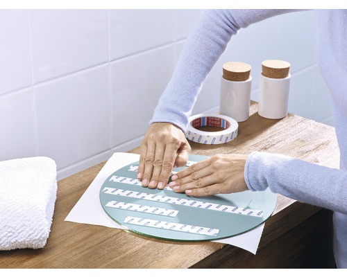 Een persoon bevestigt spiegeltape op een ronde spiegel op een tafel.