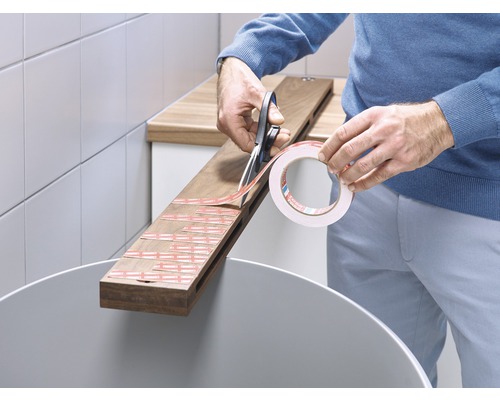 Een persoon knipt dubbelzijdig plakband met een schaar op een houten plank.