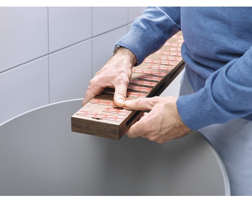 Man houdt houten plank met plakstrips boven een container