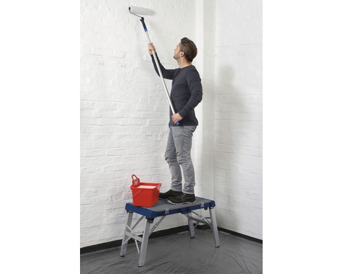 Man schildert een muur met een verfroller vanaf een werkplatform.