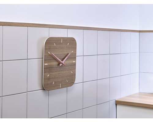 Houten wandklok met roze wijzers aan betegelde muur