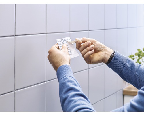 Man bevestigt een plakstrip aan een wand met tegels