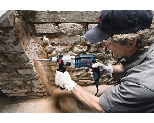 Man boort met een klopboormachine een gat in een bakstenen muur. Bosch Logo.