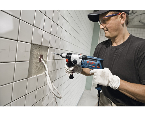 Man boort met een klopboormachine een gat in een betegelde muur.