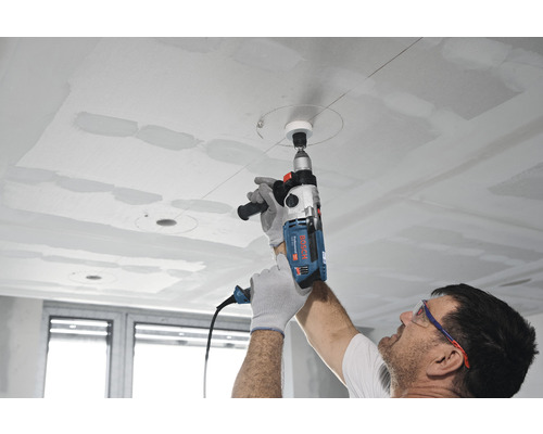 Een persoon boort met een boormachine een gat in een plafond.
