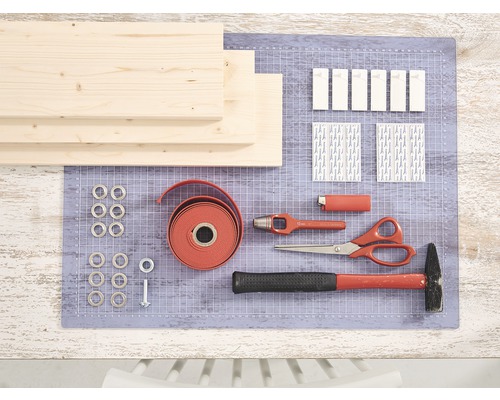 Diverse knutselmaterialen en gereedschappen op een werkoppervlak, waaronder houten planken, oogjes, een rode band, schroeven, plakstrips, een hamer, een schaar en een pons.