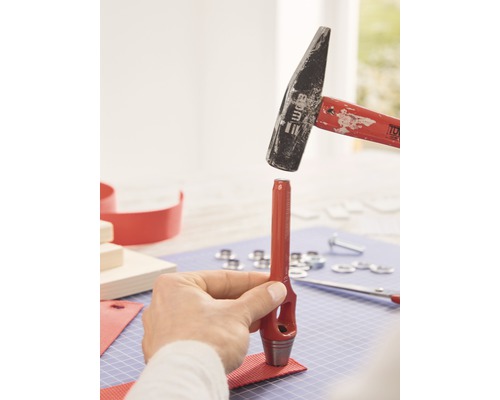 Een persoon gebruikt een hamer en een pons om een gat in een stuk stof te slaan.