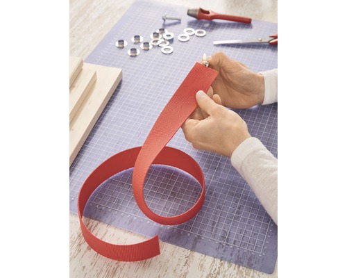 Persoon smelt het uiteinde van een textielband met een aansteker, gereedschap en oogjes liggen op een snijmat