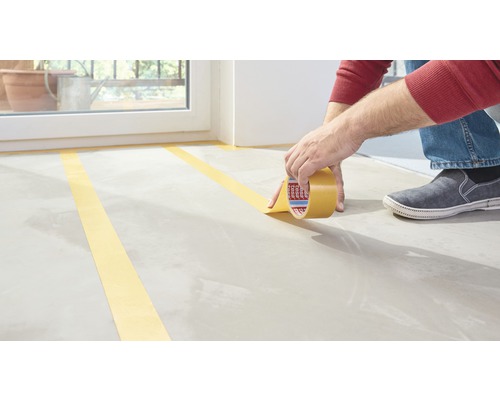 Persoon plakt schilderstape op een vloer.