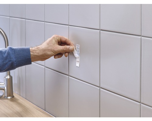 Een persoon bevestigt een plakstrip aan een betegelde muur.