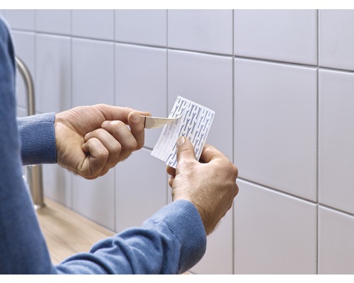 Iemand verwijdert de beschermfolie van een plakstrip voor een betegelde wand.