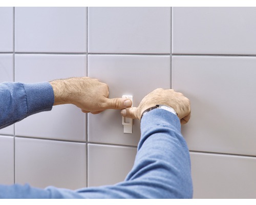 Iemand bevestigt een tegelnivelleerder aan een betegelde muur.