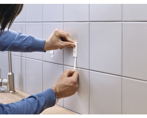 Persoon bevestigt een tegelnivelleringssysteem aan een betegelde muur