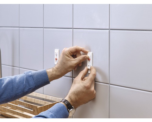 Montage van twee zelfklevende haken op tegels op de muur