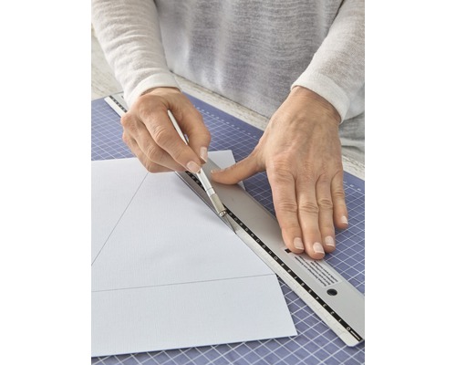 Persoon snijdt papier met mes en liniaal op een snijmat