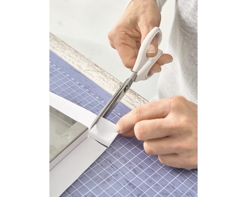 Persoon knipt met een schaar een witte band op een snijmat