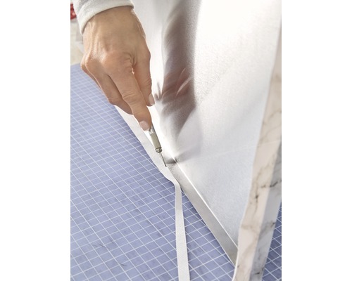 Een persoon snijdt met een mes een beschermfolie op een werkblad.