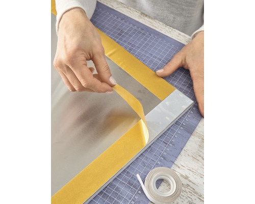 Persoon bevestigt spiegel met dubbelzijdige tape op een snijmat.