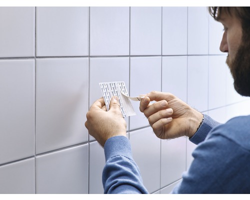 Persoon verwijdert beschermfolie van plakstrips voor witte tegels