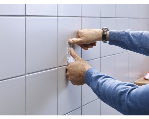 Dubbelzijdige tape wordt aan een wandtegel bevestigd.