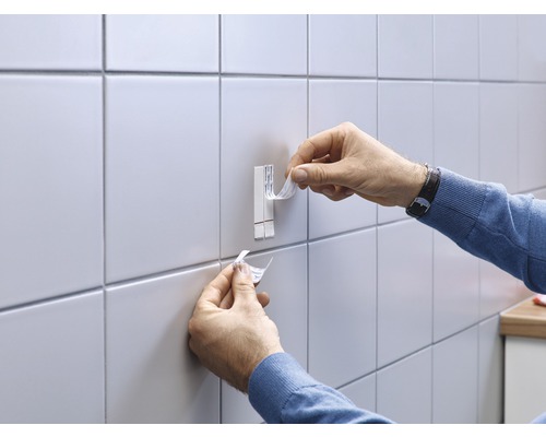 Persoon bevestigt een zelfklevende haak aan een betegelde muur.