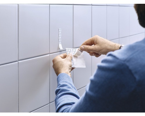 Man bevestigt plakstrips op de tegelmuur