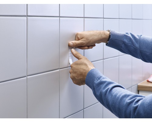 Toepassing van plakstrips op tegels door een persoon