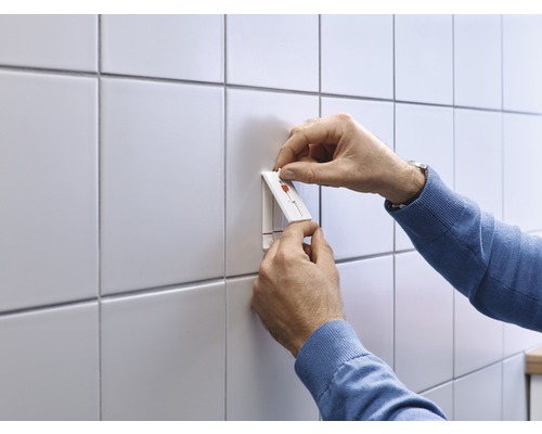 Persoon bevestigt een zelfklevende haak aan een betegelde muur