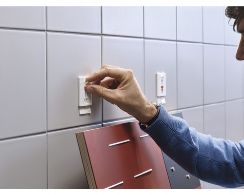 Persoon bevestigt een zelfklevende haak aan een betegelde muur