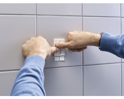 Persoon bevestigt een zelfklevende haak aan een betegelde muur.