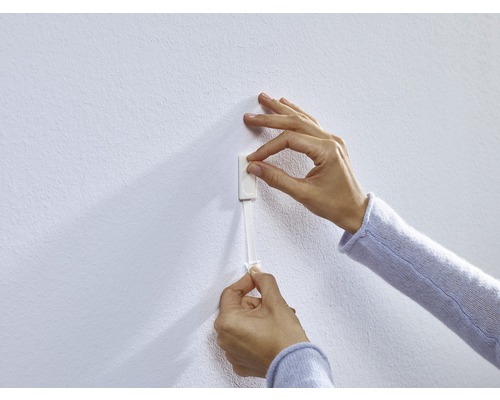 Een persoon bevestigt een zelfklevende strip aan een muur.