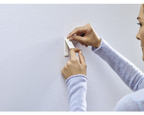 Vrouw bevestigt een zelfklevende haak aan de muur