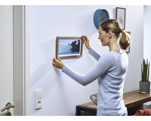 Vrouw hangt fotolijst aan de muur in een woonkamer