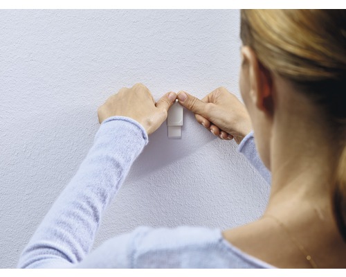 Vrouw bevestigt een zelfklevende haak aan de muur