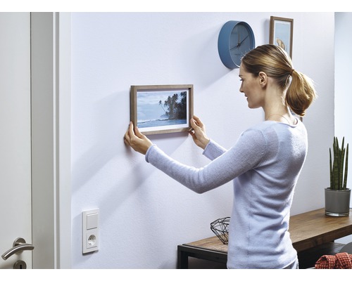 Vrouw hangt een foto met houten frame aan de muur