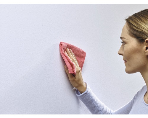 Een vrouw maakt een muur schoon met een doek.