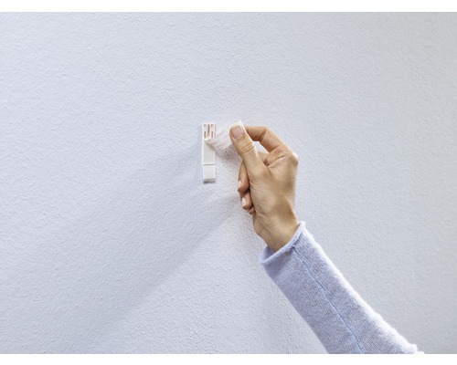 Een hand bevestigt een zelfklevende fotolijsthaak aan een muur.