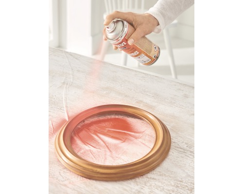 Een persoon spuit verf op een fotolijst met een spuitbus.