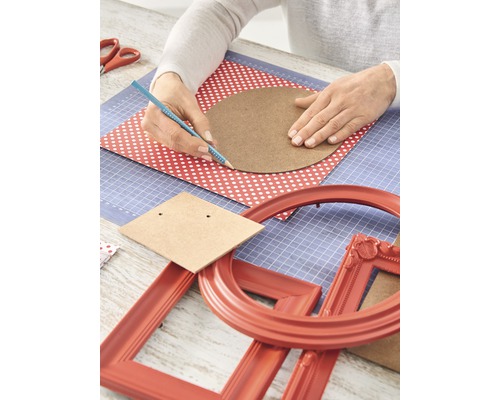 Knutseltafel met handen die een cirkel op een vel papier tekenen, omringd door knutselmateriaal en fotolijsten