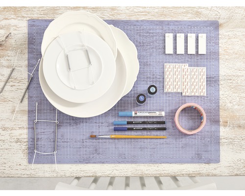 Scene met borden, bordenhouders, porseleinverf, penselen, plakband en bevestigingsmateriaal op een snijmat