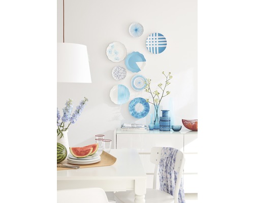 Lichte eetkameropstelling met decoratief servies aan de muur, fruit en servies op tafel en decoratieve vazen op het dressoir.