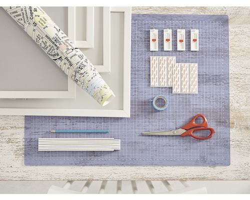 Scene met fotolijsten, stadsplattegrondrol, snijmat, plakstrips, plakband, potlood, duimstok en schaar.