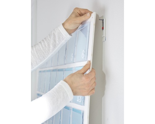 Handen monteren een adventskalender met vakken aan de wand.