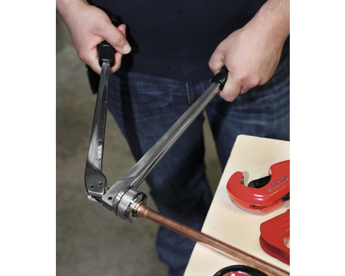 Een persoon gebruikt een perstang om een koperen buis te persen.