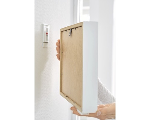 Een persoon bevestigt een fotolijst met een zelfklevende spijker aan een muur.