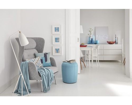 Woonkamer met fauteuil, staande lamp en poef in een lichte, vriendelijke sfeer.